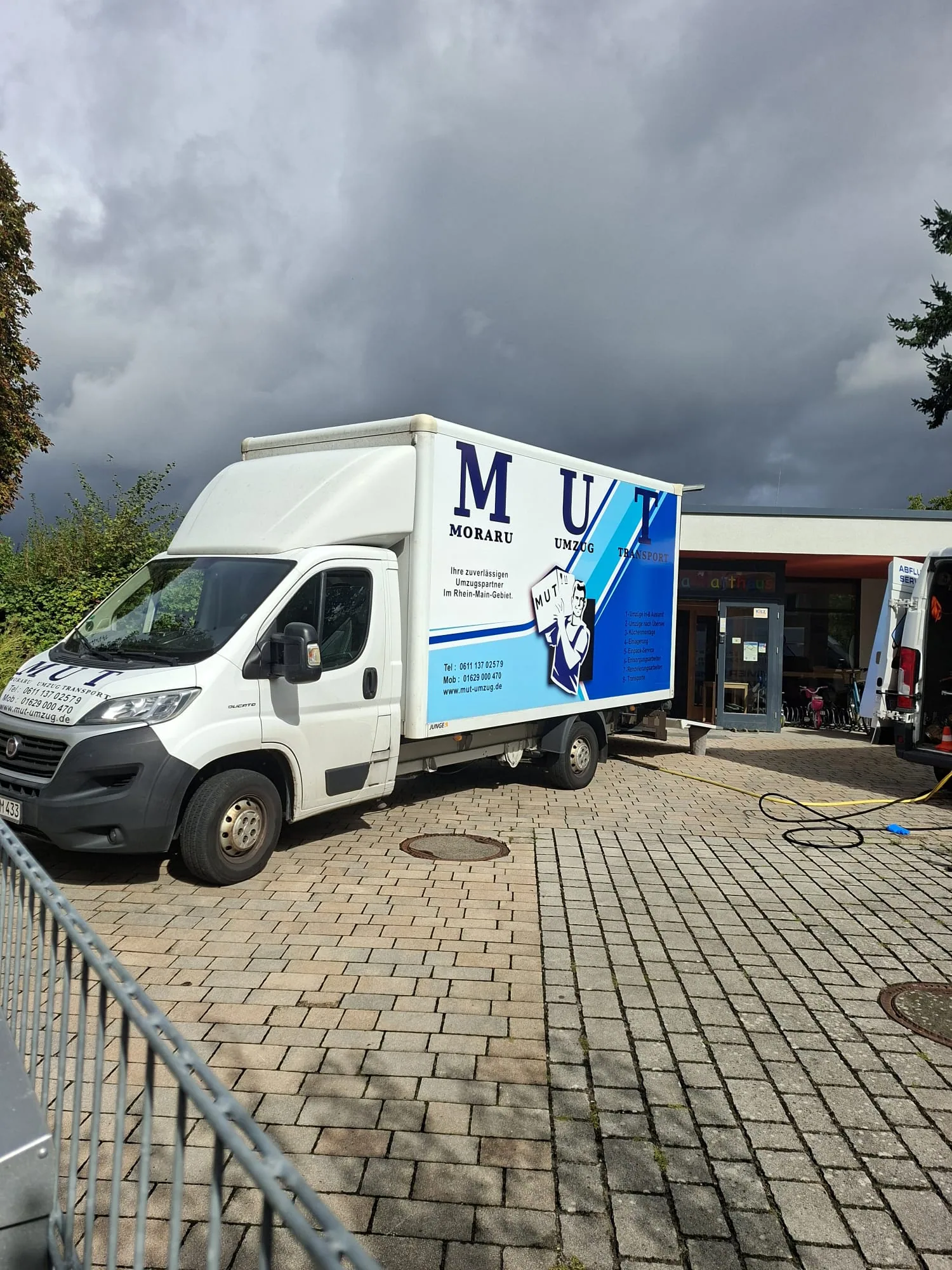 MUT-Umzugswagen mit abgesenkter Ladebordwand vor einem Gemeindezentrum