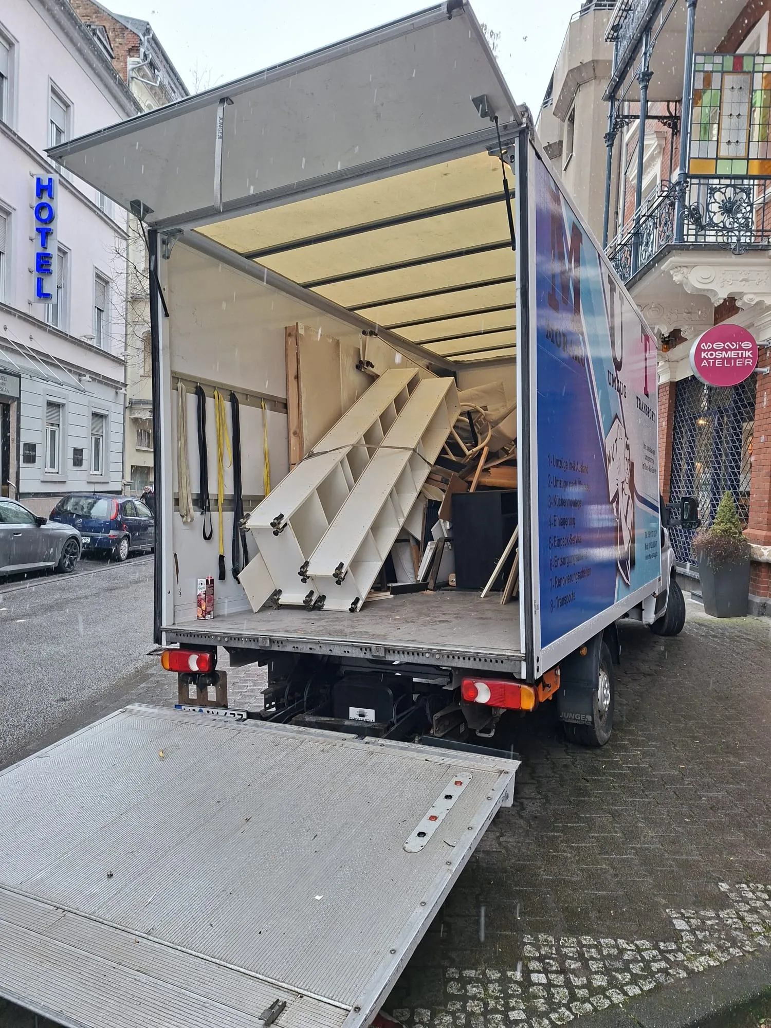 Geöffneter MUT-Umzugswagen mit Ladebordwand vor einem Hotel