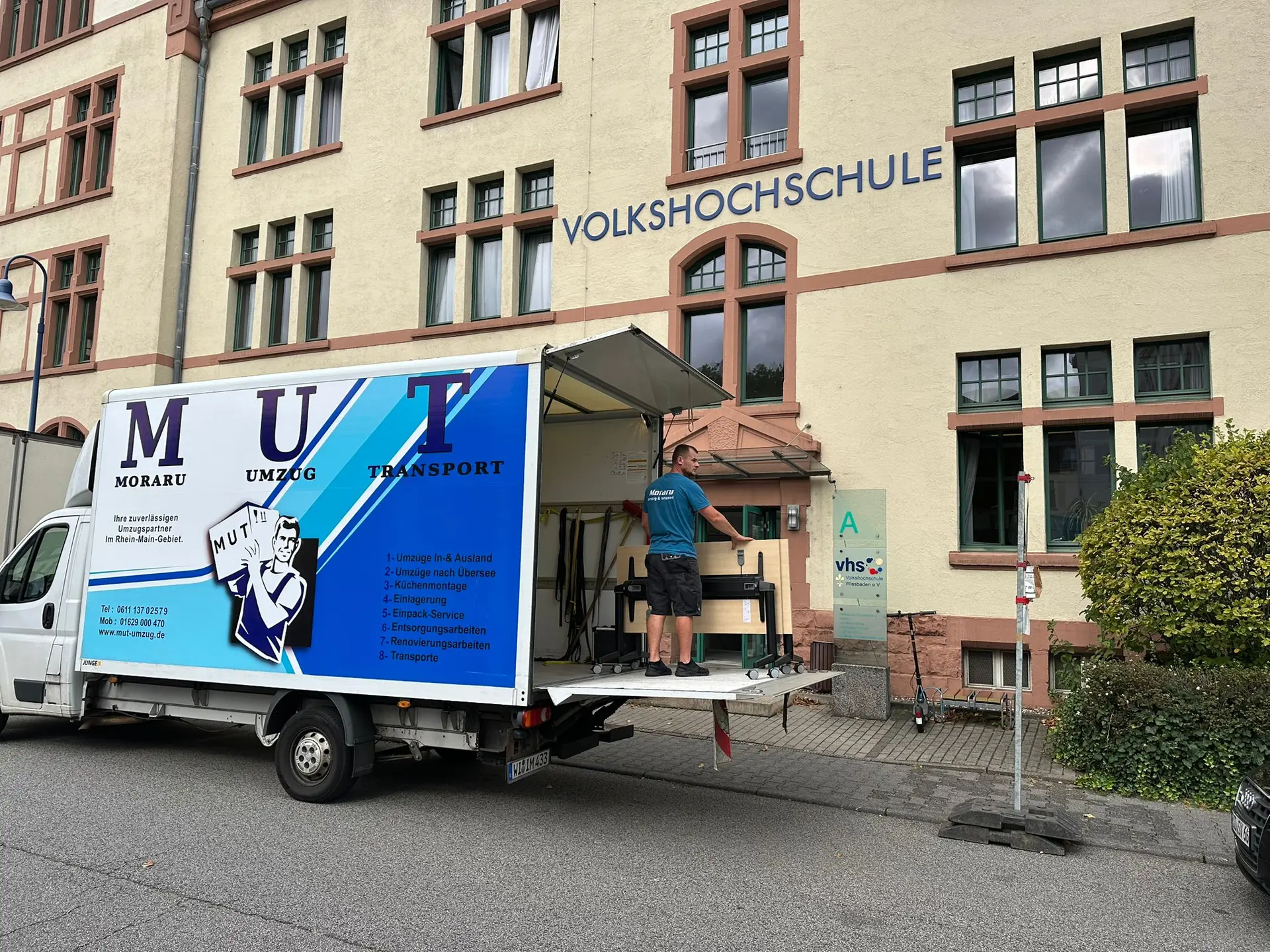 MUT-Umzugswagen mit geöffneter Ladebordwand vor einer Volkshochschule