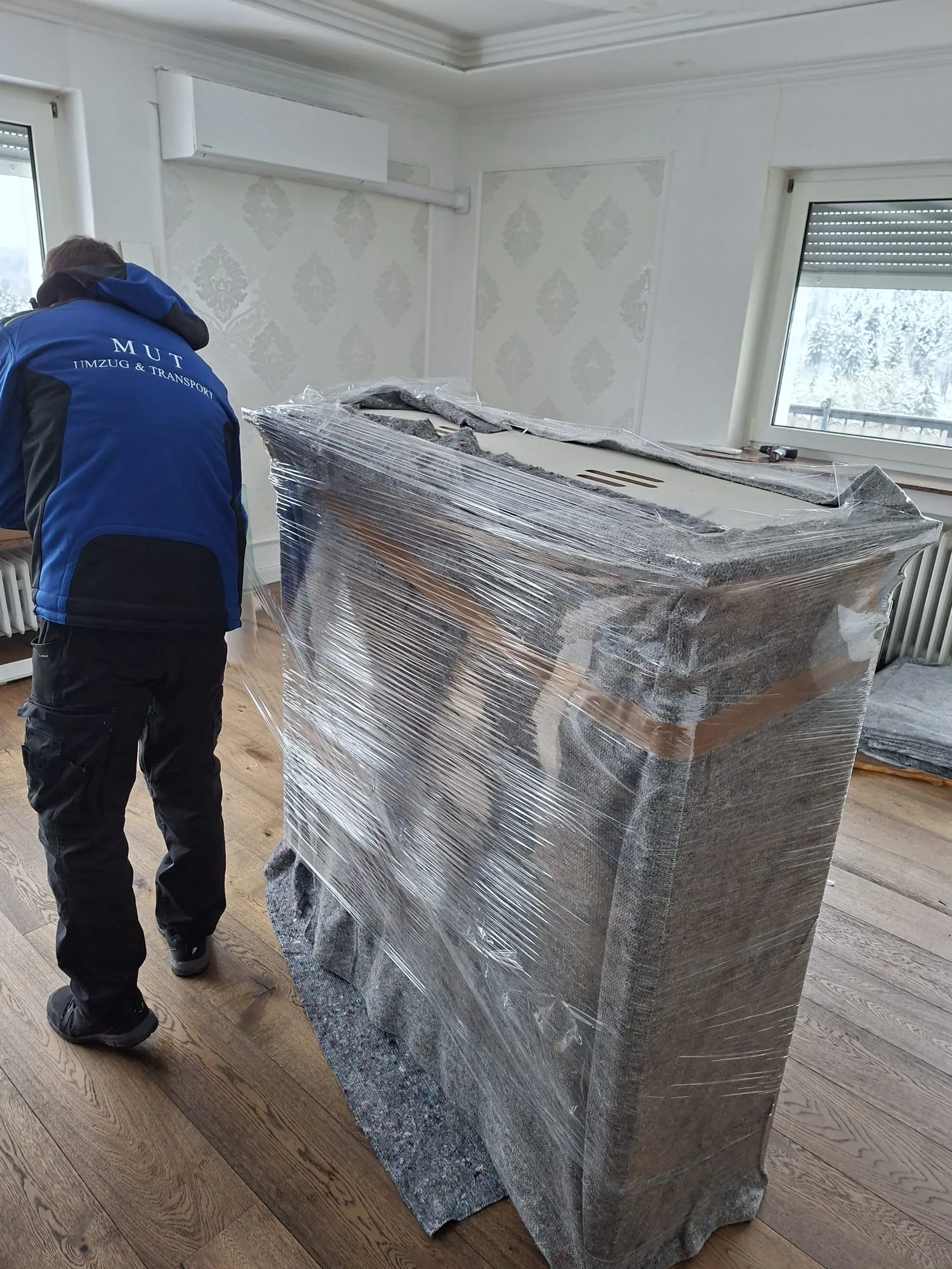 MUT-Mitarbeiter schiebt ein in Stretchfolie verpacktes Möbelstück durch eine Altbauwohnung